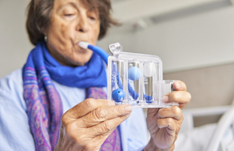 spirometer for breathing exercises. senior woman in hospital room practicing with spirometer
